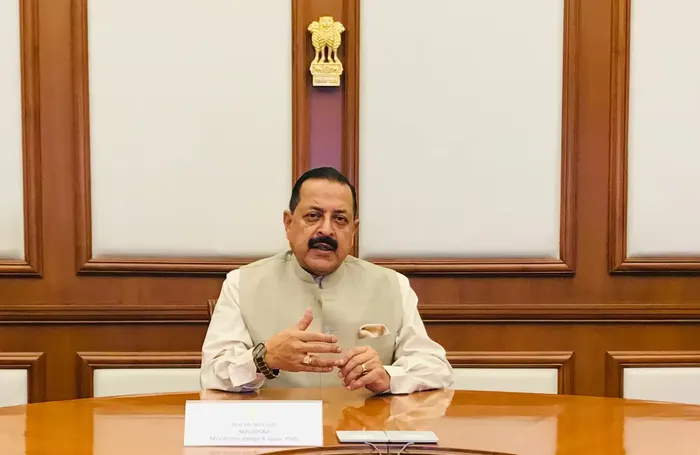 Dr. Jitendra Singh seated at a polished table in a wood-panelled room beneath the national emblem