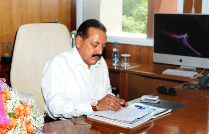 Dr. Jitendra Singh signing papers at an office desk beside flowers