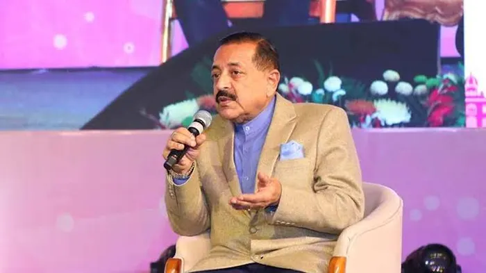 Dr. Jitendra Singh seated on stage holding a microphone