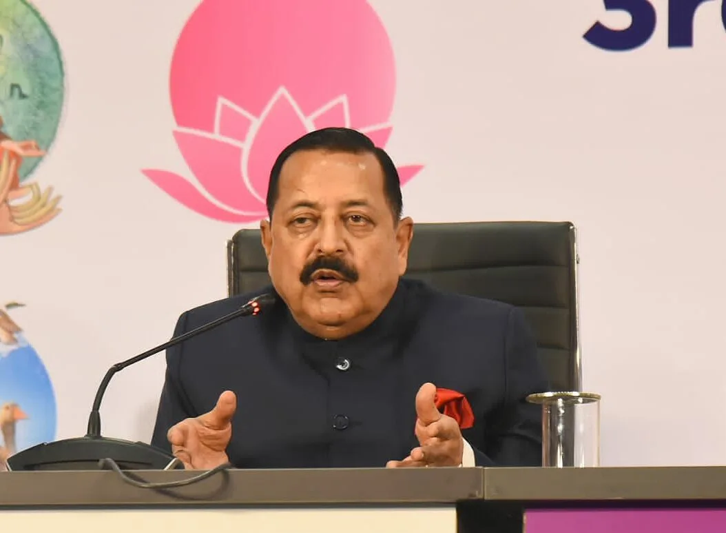 Dr. Jitendra Singh seated at a press conference table with a microphone, gesturing with both hands