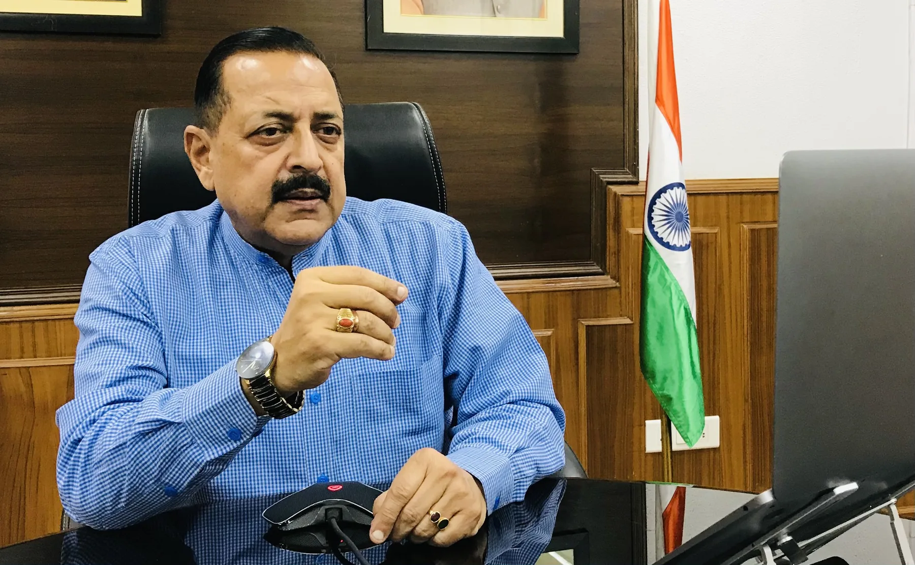 Dr. Jitendra Singh seated at his office desk beside the national flag, gesturing while speaking