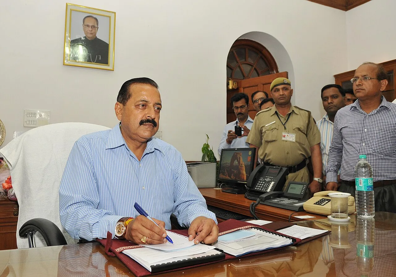 Dr. Jitendra Singh signing papers at a desk, with officials standing behind him