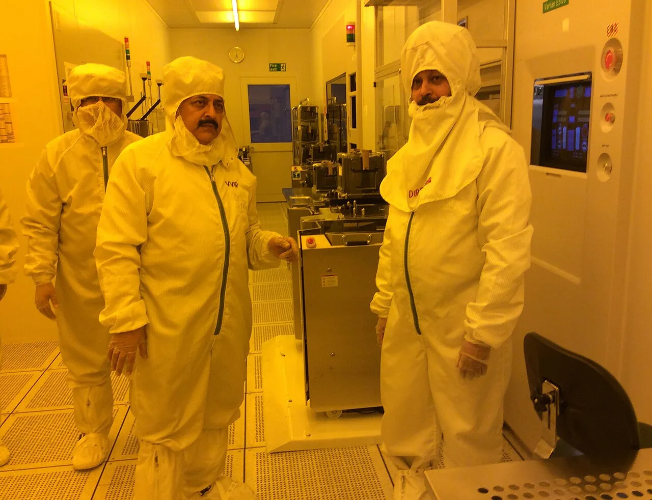 Dr. Jitendra Singh and two others in full cleanroom suits inside a semiconductor fabrication laboratory lit in amber